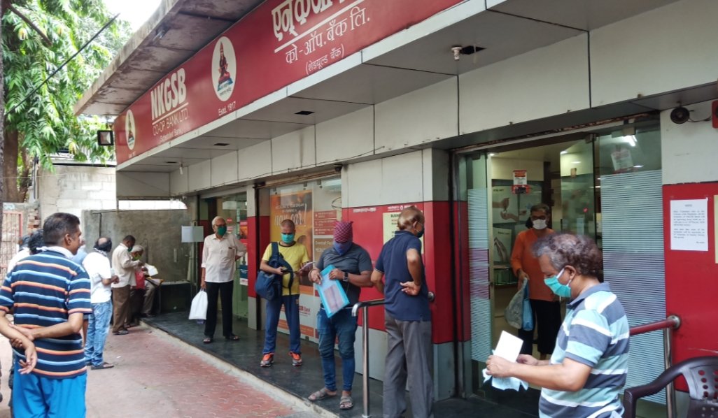 Adarsh Maharashtra | बँकेबाहेरील भल्या मोठ्या रांगेत उन्हात उभे राहावे लागत असल्याने रांगेतील...